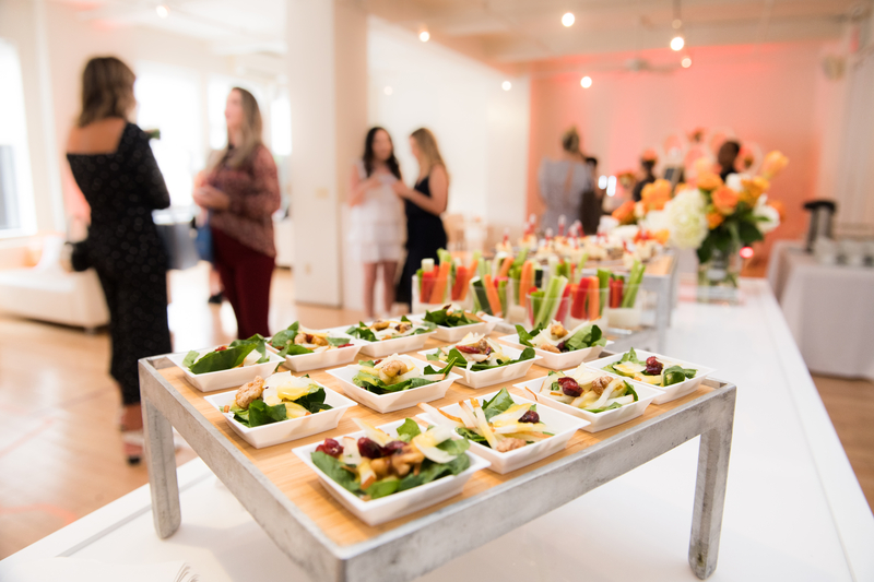 People gathering for an event with appetizers neatly laid out on a long table with a white linen cloth.