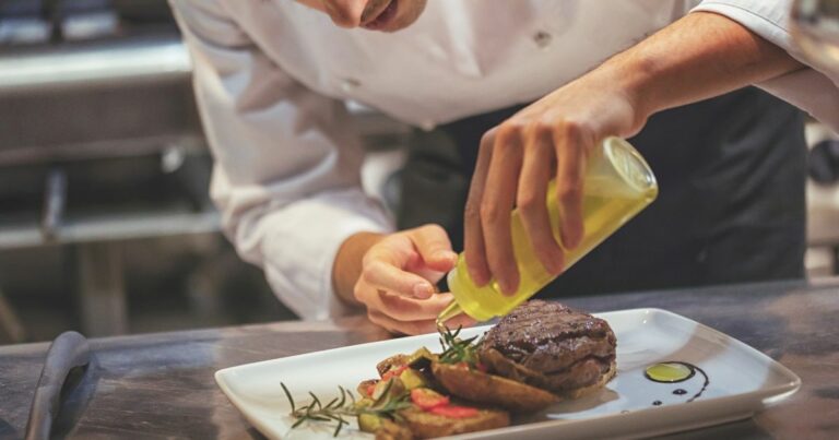 Upclose image of a chef in a white coat adding olive oil to a meal